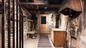 Un estrecho pasillo de paredes de piedra con una puerta de madera, un banco y una pequeña mesa de madera.