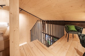 A wooden interior with a staircase, a green upholstered chair, and a bed with white bedding. - Historic Chalet Raneburg (Matrei in Osttirol)