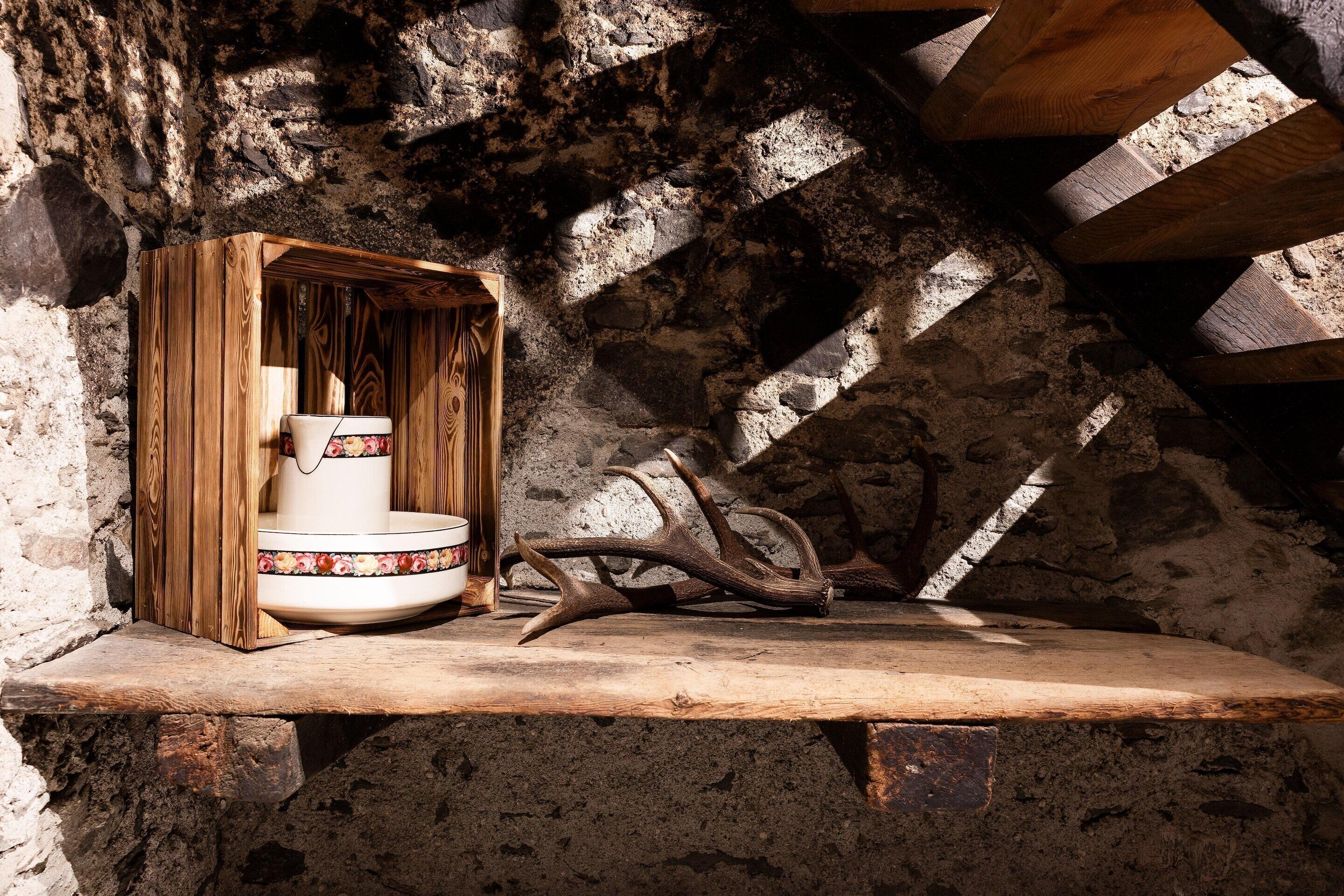 A rustic interior with a wooden shelf, a white ceramic basin, and antlers.