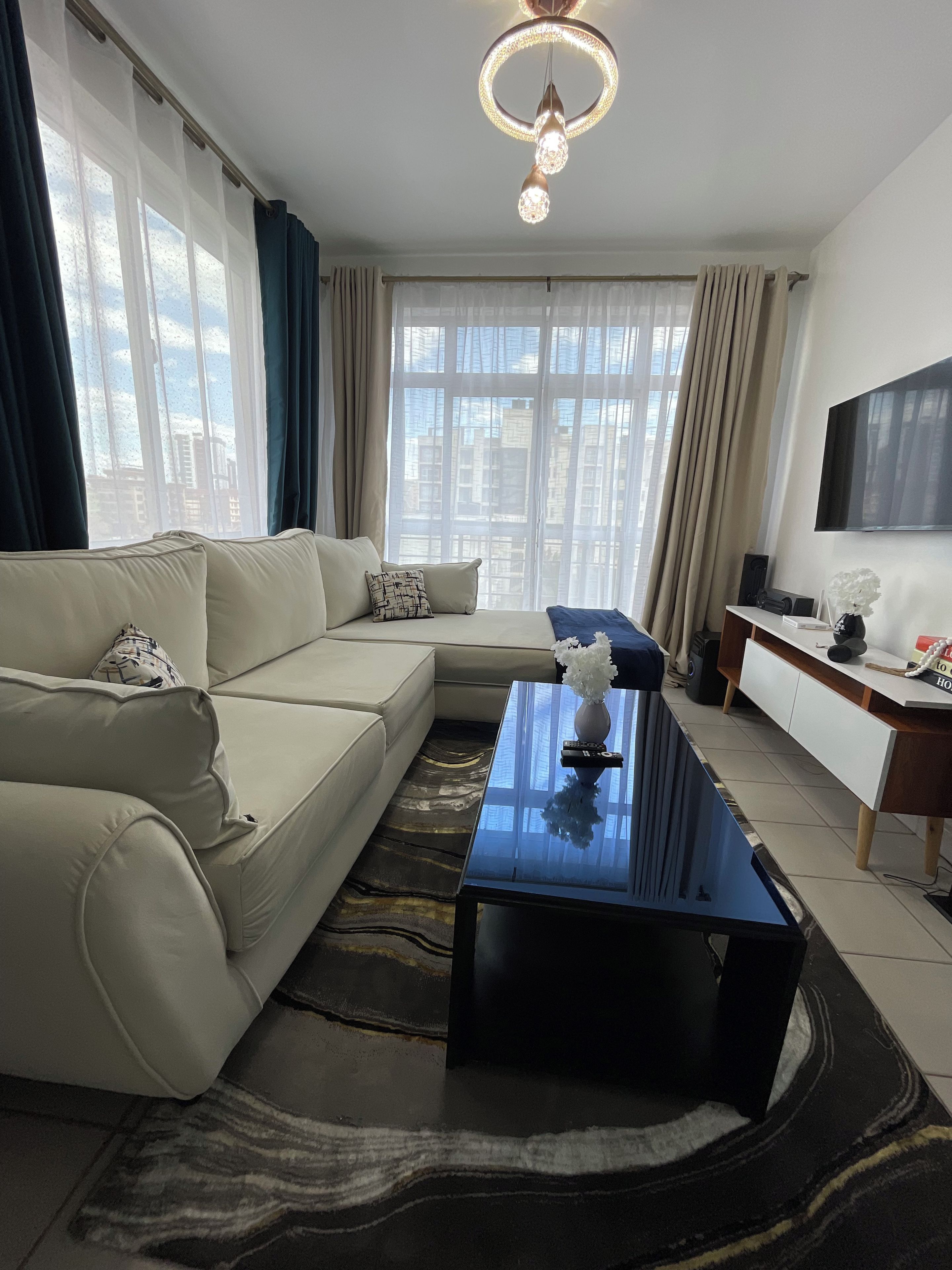Ein modernes Wohnzimmer mit einer Eckcouch, einem Couchtisch, einem Flachbildfernseher und einem großen Fenster mit Vorhängen.