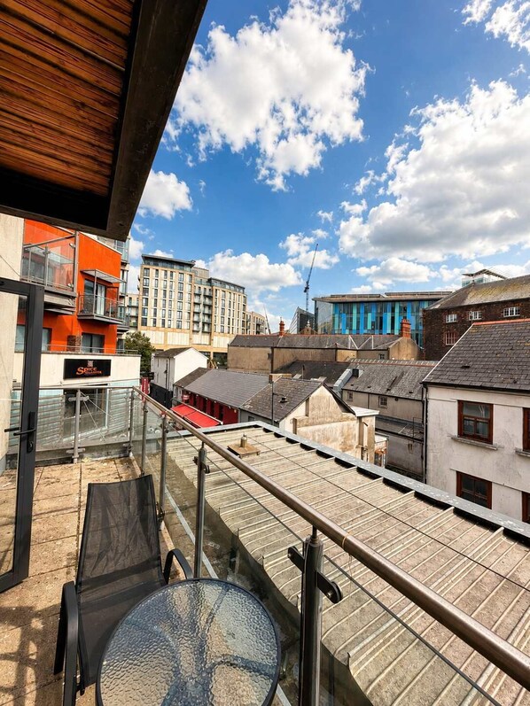 A rooftop terrace with a glass table and chairs, overlooking a cityscape with modern buildings. - Cardiff City Centre 2-Bed, 2-Bath Flat | Balcony | Coopers Court (Cardiff)