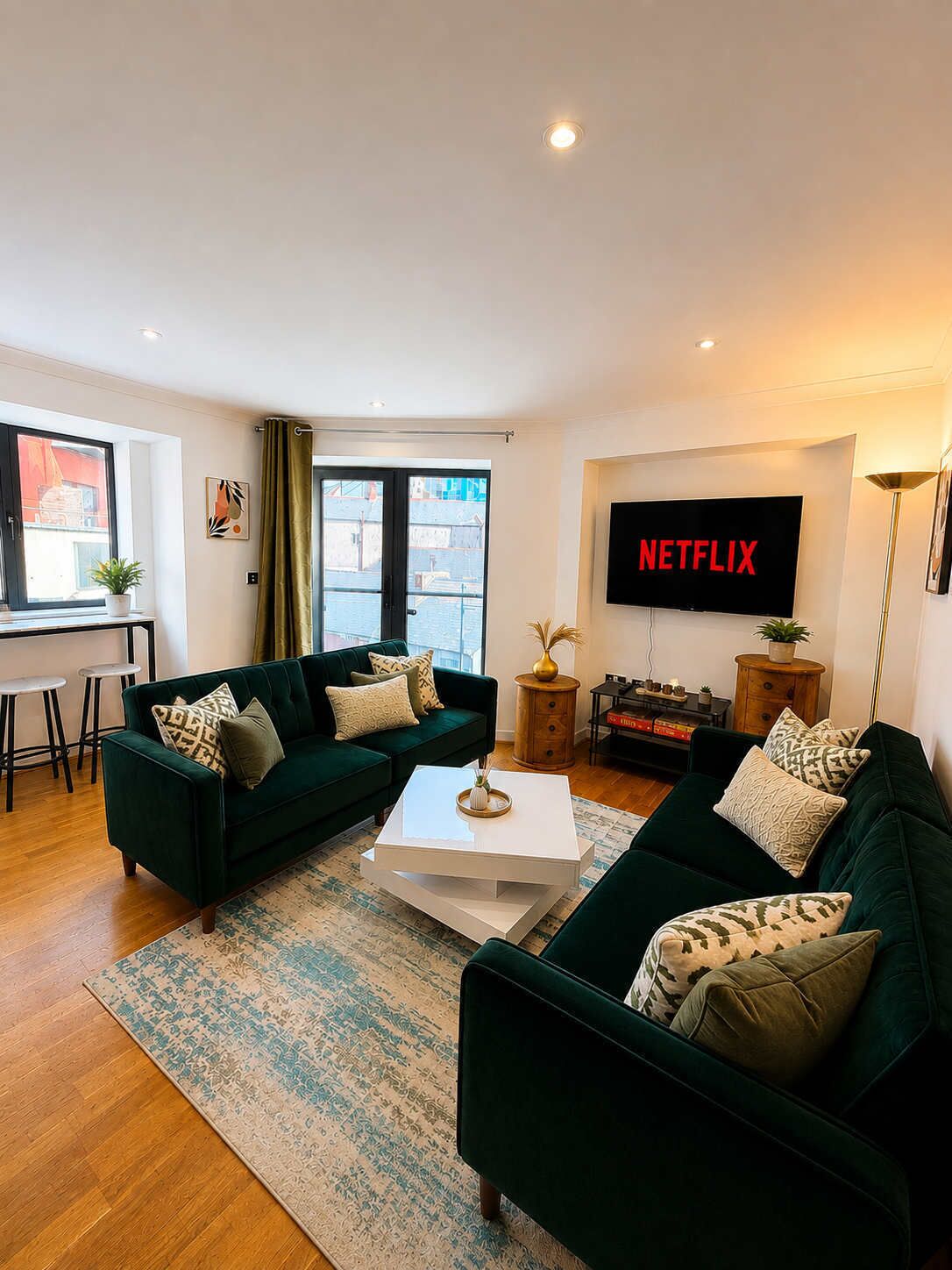 Una sala de estar moderna con dos sofás verdes, una mesa de centro, un televisor de pantalla plana y un ventanal con cortinas.