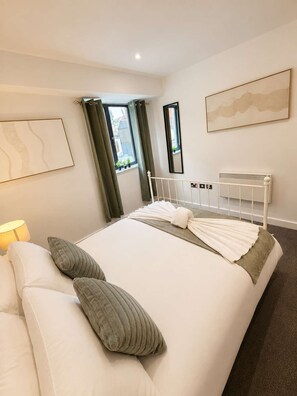A hotel room with a bed, bedside table, lamp, and a view of the outside. - Cardiff City Centre 2-Bed, 2-Bath Flat | Balcony | Coopers Court (Cardiff)