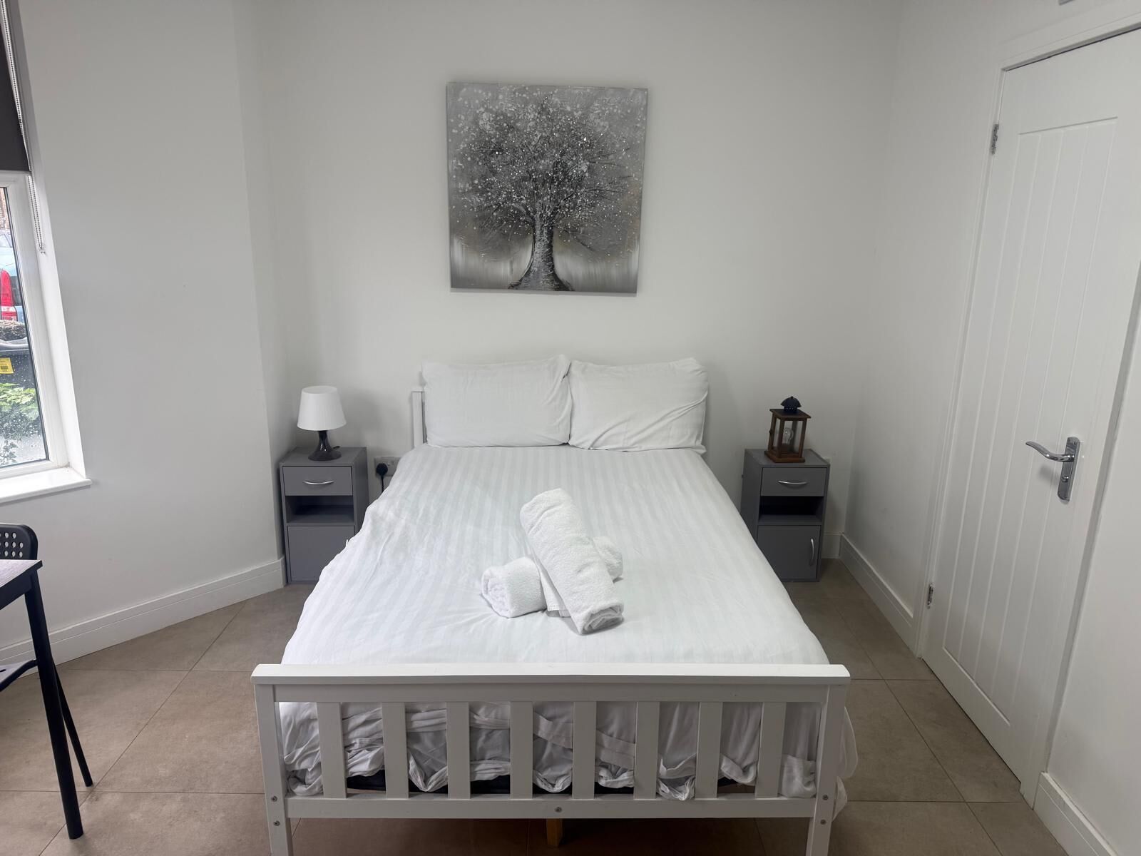 A bedroom with a bed, two bedside tables, a nightstand, a window, and a door.
