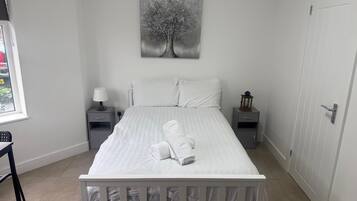 A bedroom with a bed, two bedside tables, a nightstand, a window, and a door.