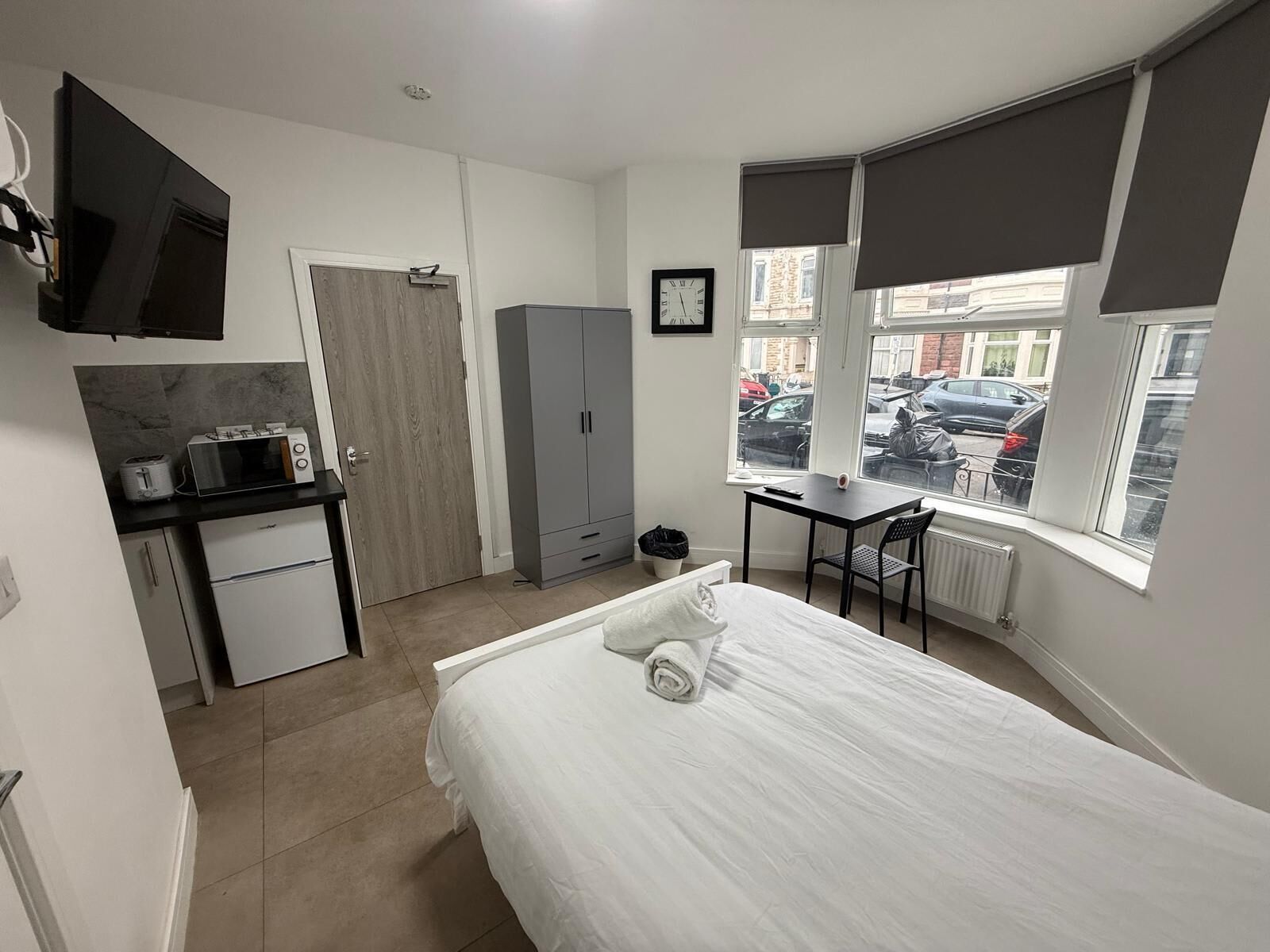 A compact bedroom with a bed, a desk, a wardrobe, and a television.