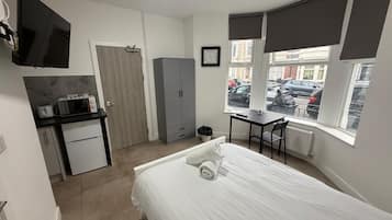A compact bedroom with a bed, a desk, a wardrobe, and a television.