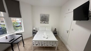 Ett sovrum med en säng, ett skrivbord, en stol, ett nattduksbord, en lampa, en tavla och en tv som är monterad på väggen.