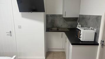 Cocina compacta con estufa a gas integrada, un lavamanos y armarios blancos.