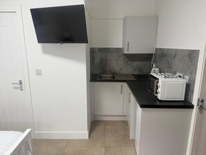 A compact kitchen with a built-in gas stove, a sink, and white cabinets. - Cozy Studio Flat - With Garden and Modern Amenities (Cardiff)