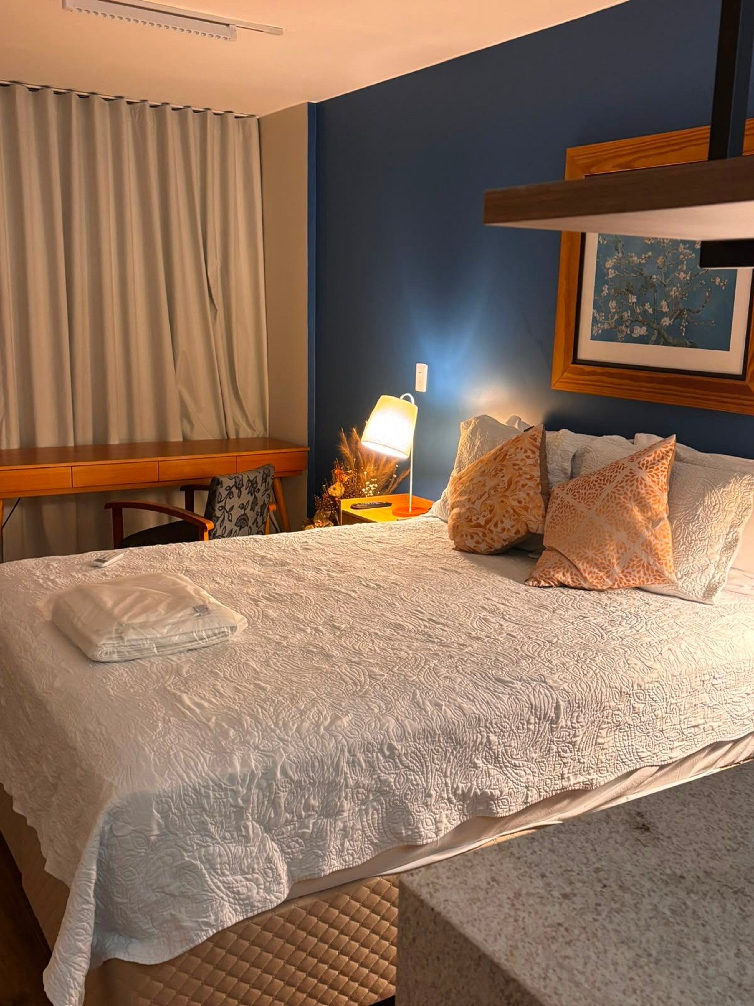 Ein Hotelzimmer mit einem großen Bett, einem Schreibtisch, einer Lampe und einem gerahmten Bild an der Wand.