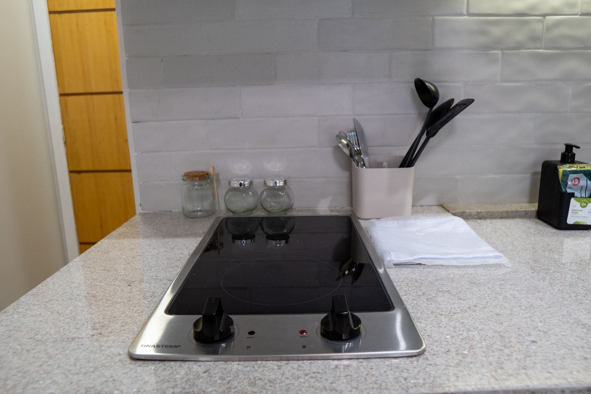 Una cocina con estufa de acero inoxidable, tres frascos de vidrio, un organizador de especias y un dispensador de jabón.