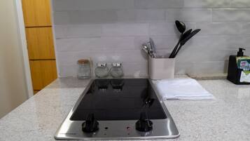 Una cocina con estufa de acero inoxidable, tres frascos de vidrio, un organizador de especias y un dispensador de jabón.