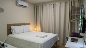 Een hotelkamer met een bed, een bureau met een laptop, een koffer en een kapstok.