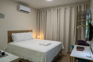 A hotel room with a bed, a desk with a laptop, a suitcase, and a hanging coat rack. - CLN 308 B Asa Norte (Brasília)