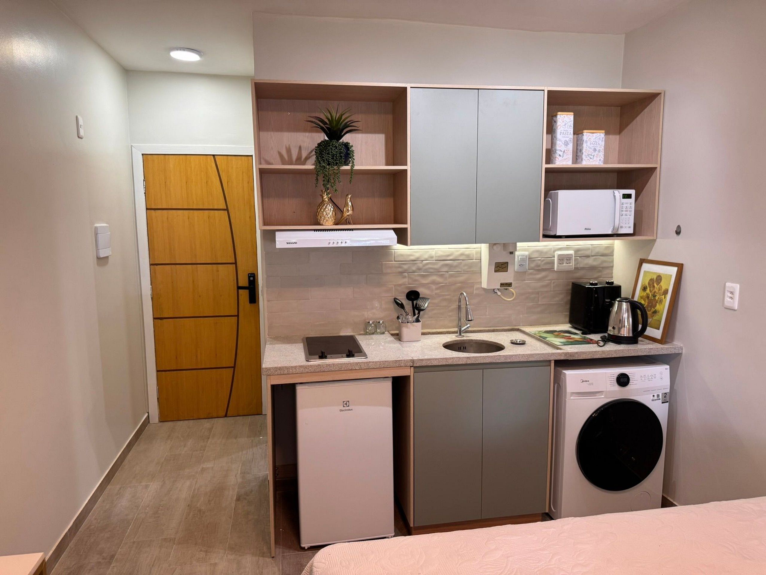 Una kitchenette compacta con lavavajillas integrado, un microondas y un lavamanos pequeño.