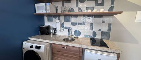 A compact kitchenette with a washing machine, a coffee maker, and a refrigerator.