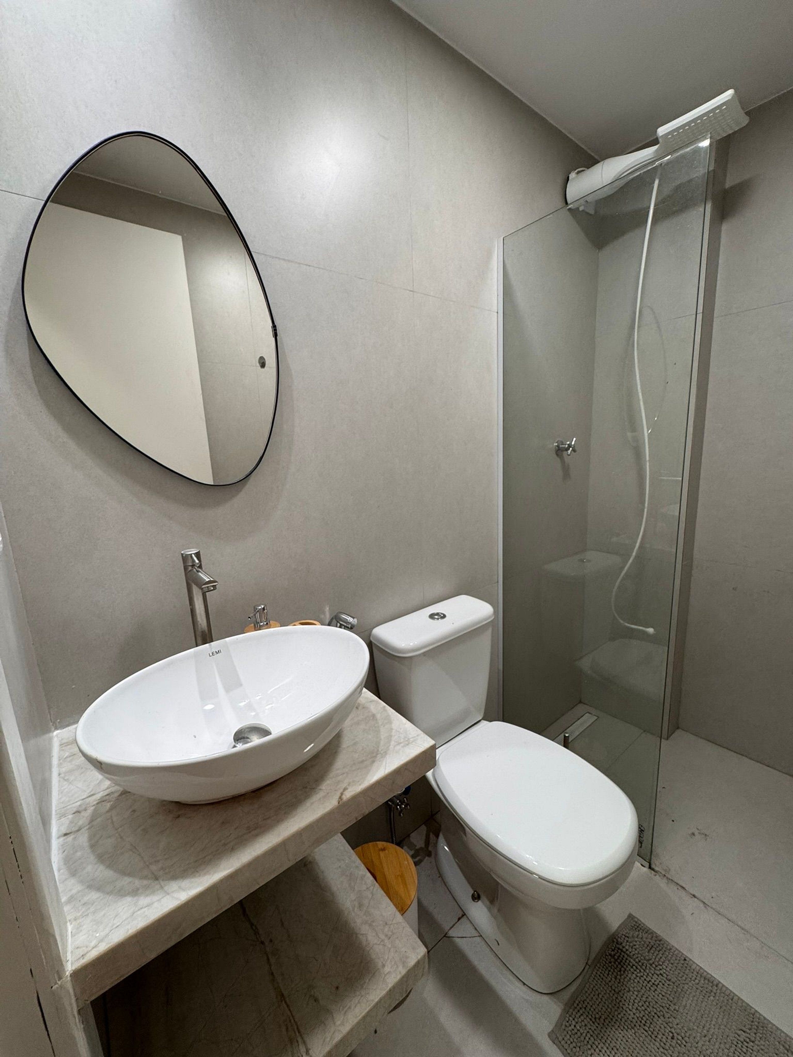 A bathroom with a round mirror, a white sink, a toilet, and a glass-enclosed shower.