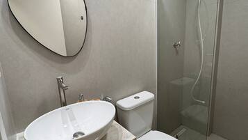 A bathroom with a round mirror, a white sink, a toilet, and a glass-enclosed shower.
