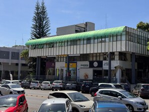 A multi-story building with a green roof, various storefronts, and parked cars in front. - CLN 308 B Asa Norte (Brasília)