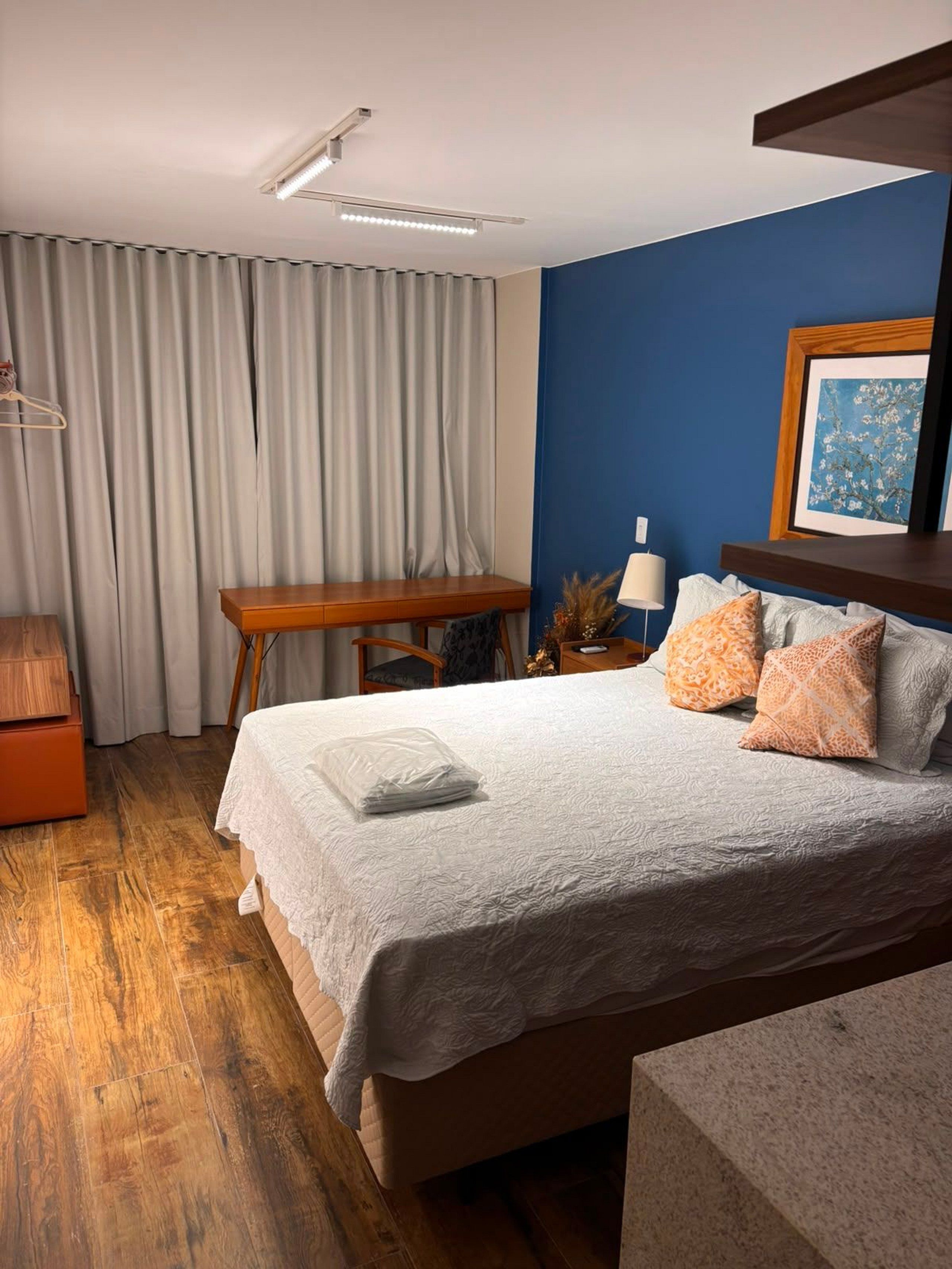 A hotel room with a bed, a desk, a chair, a lamp, and a framed picture on the wall.