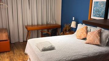 A hotel room with a bed, a desk, a chair, a lamp, and a framed picture on the wall.