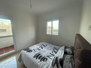 A bedroom with a bed, a window, and a view of buildings outside.