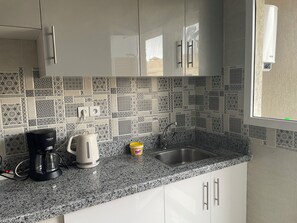 A kitchen with white cabinets, a granite countertop, a coffee maker, a kettle, and a sink.