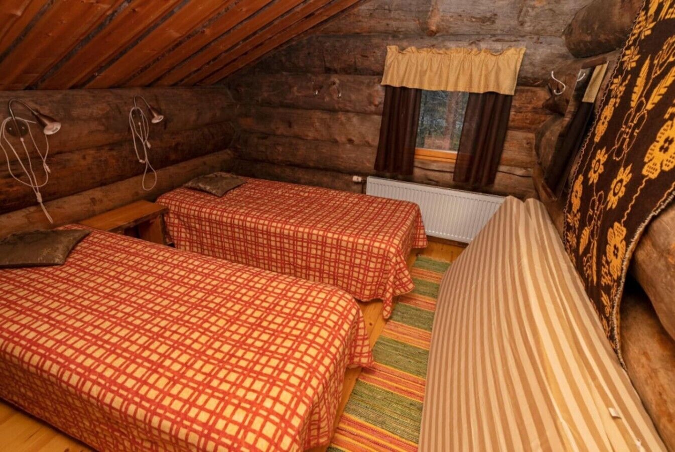 Habitación tipo cabaña de madera con dos camas, un sofá, una ventana con cortinas y un radiador.