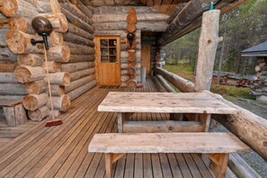 Eine Blockhütte mit einer Holzdachterrasse, einer Bank und einer Tür.