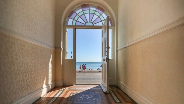 A hallway with a patterned floor leading to a door with a view of the beach. - 123 On The Sea - The Cubby (Weymouth)