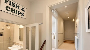 A hallway leading to a bathroom with a toilet, sink, and shower. There is a sign on the wall that reads 'FISH & CHIPS'. - 123 On The Sea - The Cubby (Weymouth)
