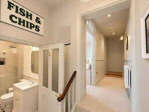A hallway leading to a bathroom with a toilet, sink, and shower. There is a sign on the wall that reads 'FISH & CHIPS'. - 123 On The Sea - The Cubby (Weymouth)