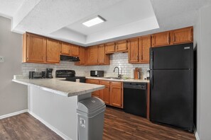 Eine moderne Küche mit Holzausstattung, einem schwarzen Kühlschrank und einem integrierten Geschirrspüler.