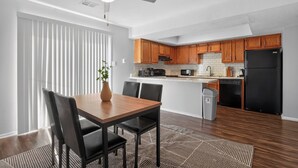 Eine moderne Küche mit Holzschränken, einem schwarzen Kühlschrank und einem Essbereich mit Tisch und Stühlen.