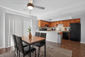 Eine moderne Küche mit Holzschränken, einem schwarzen Kühlschrank und einem Essbereich mit Tisch und Stühlen.