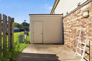A small, single-story building with a beige exterior, a wooden fence, and a paved driveway. - Comfortable 2BR Retreat at Country Lakes (Indianapolis)