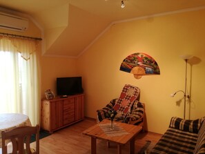 Ein Wohnzimmer mit einem Holzkabinett, einem Fernseher, einem karierten Sofa und einem Wandventilator.