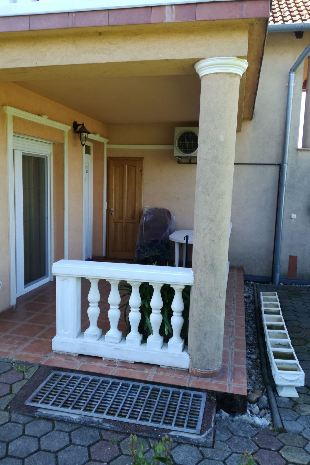 A covered outdoor area with a white balustrade, a concrete column, a door, and an air conditioning unit.