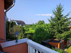 Ein Balkon mit Blick auf eine grüne Landschaft, ein Haus und eine Holzkonstruktion.