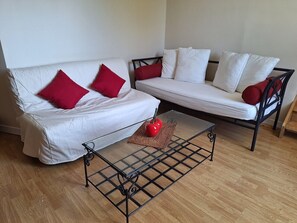A living room with a white sofa, red cushions, a black coffee table, and a red apple on the table.