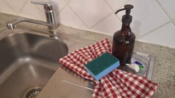 A kitchen sink with a faucet, a soap dispenser, a sponge, and a red and white checkered cloth.