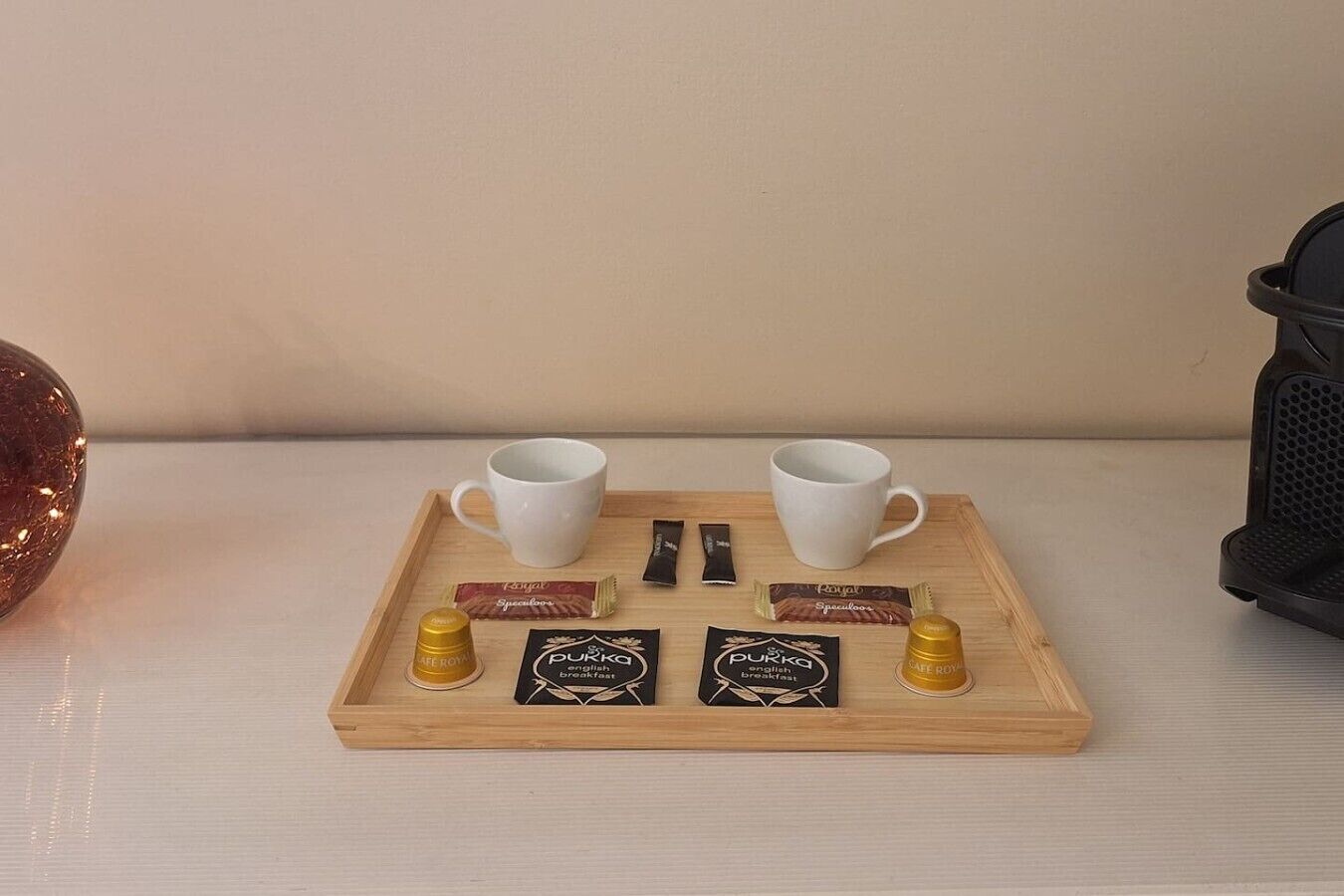 A tray with two white cups, two packets of coffee, and two small containers of cream on a wooden surface.
