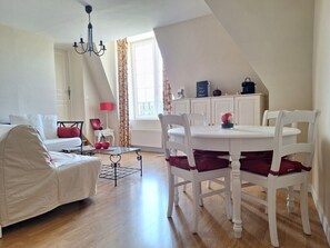 Uma sala de estar com um sofá branco, uma mesa de jantar com cadeiras brancas e um candelabro.