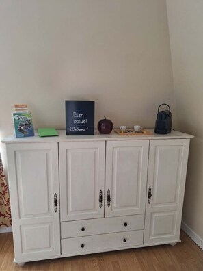 A white cabinet with drawers and doors, a chalkboard with 'Bien Venue!' written on it, a red apple, a blue bag, and a green box.