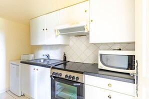 Uma cozinha compacta com fogão, micro-ondas e pia.