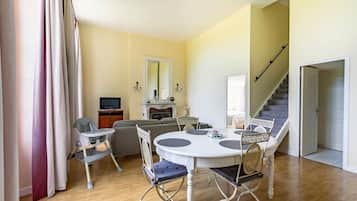 A dining area with a round table and chairs, a sofa, a television, and a staircase.
