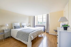 A hotel room with a large bed, bedside tables, a desk, a chair, and a window with curtains.