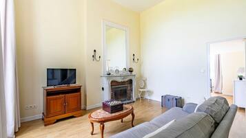 Uma sala de estar com televisão, lareira, sofá e uma pequena mesa com um jogo de xadrez.