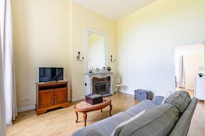 Uma sala de estar com televisão, lareira, sofá e uma pequena mesa com um jogo de xadrez.